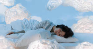 Mulher dormindo tranquilamente em uma cama macia, rodeada por um ambiente suave e relaxante, com nuvens ao fundo, simbolizando a sensação de descanso profundo e reparador.