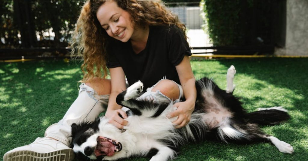 Mulher sorrindo enquanto brinca com cão em gramado, representando os benefícios dos cães de suporte emocional