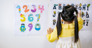 Criança em escola com uma aluna manipulando letras do alfabeto em ambiente educacional