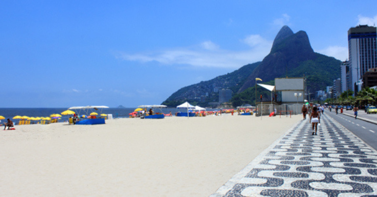 Praia de Ipanema no Rio de Janeiro em dia ensolarado com calçadão, areia clara e o Morro Dois Irmãos ao fundo