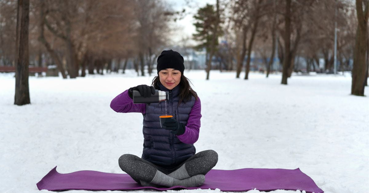 Mulher se protege durante a onda de frio praticando atividades ao ar livre com roupas térmicas e bebida quente