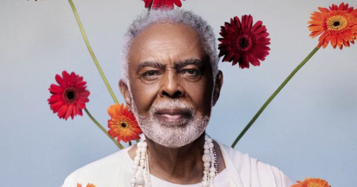 Gilberto Gil em imagem de divulgação, rodeado por flores coloridas.