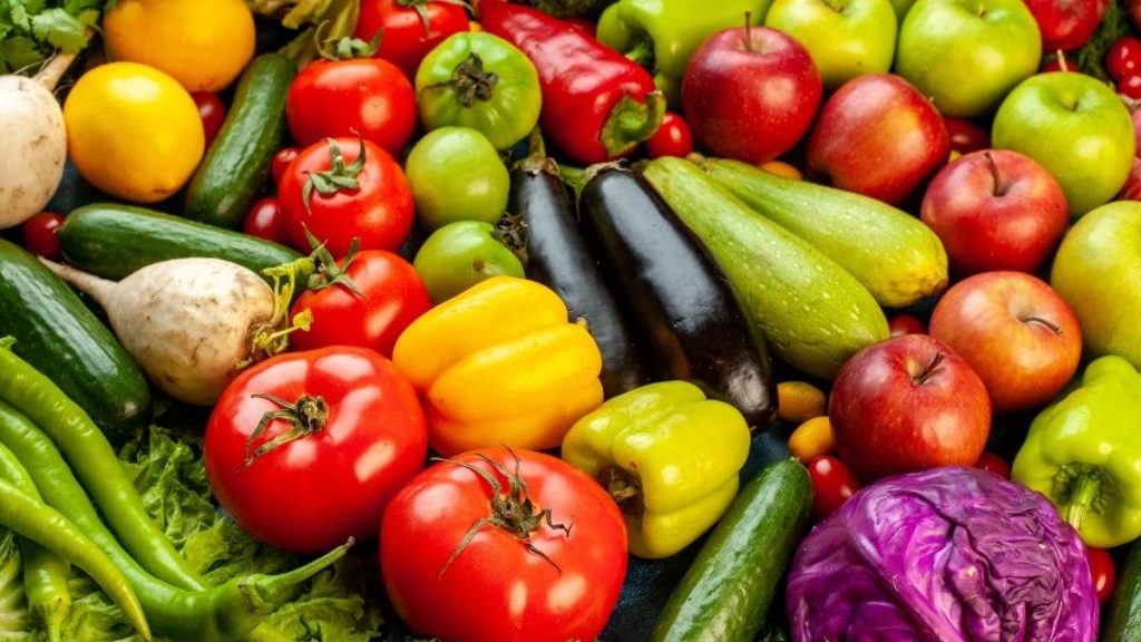Comer frutas e vegetais melhora o sono Frutas e vegetais coloridos em uma mesa ao lado de uma cama reforçam como comer frutas e vegetais melhora o sono.