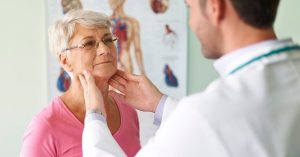 Médico examina pescoço de paciente idosa durante consulta para avaliar possíveis doenças da tireoide