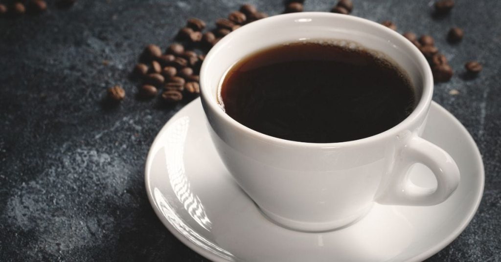 Xícara de café preto em fundo escuro com grãos ao redor