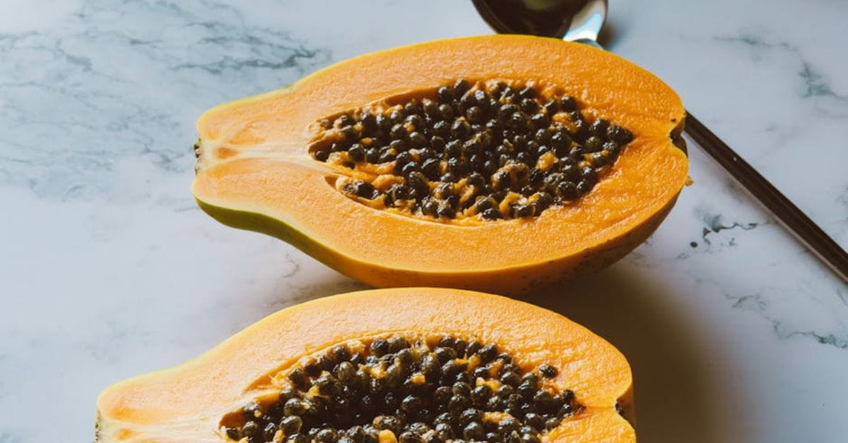 Mamão cortado ao meio com sementes expostas sobre superfície clara