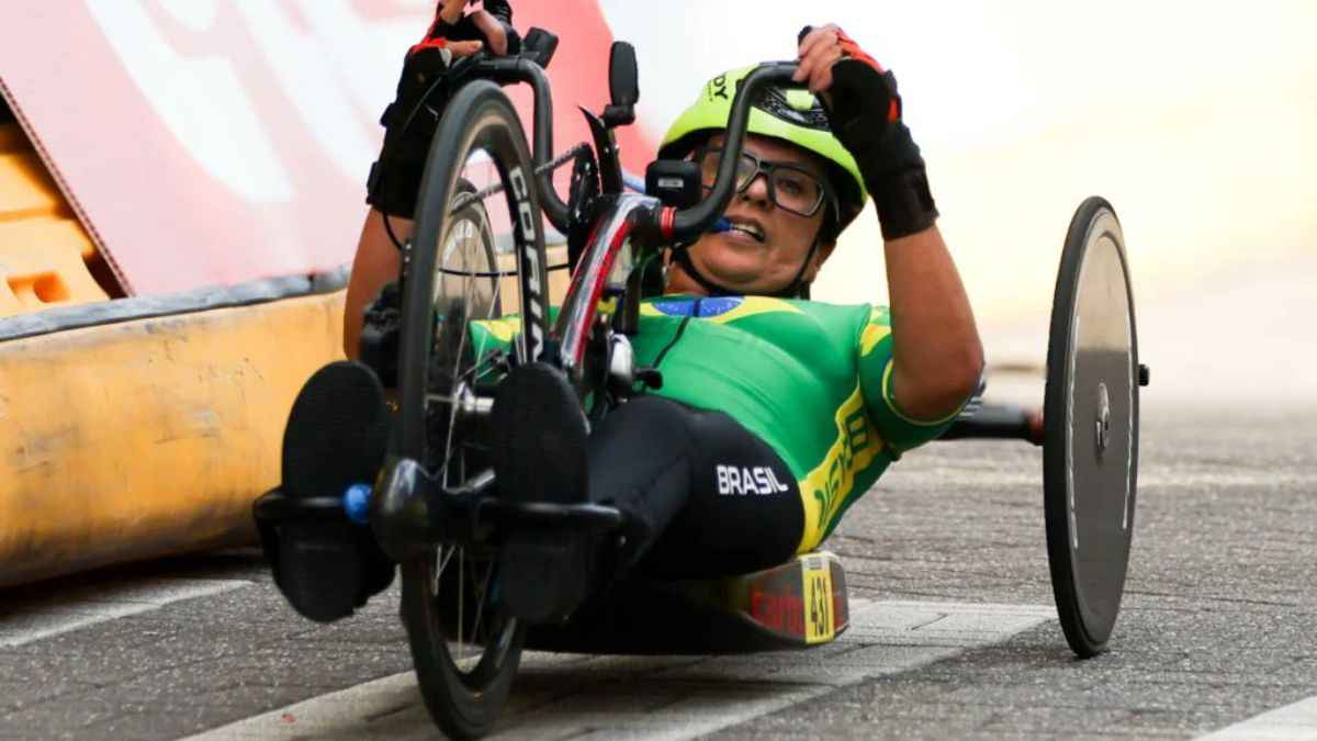 Atletas do paraciclismo brasileiro em prova internacional com bicicletas adaptadas e bandeira do Brasil em evidência.