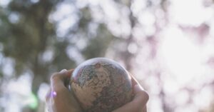 Mãos segurando um pequeno globo terrestre com fundo natural, representando a adaptação da saúde ao clima.