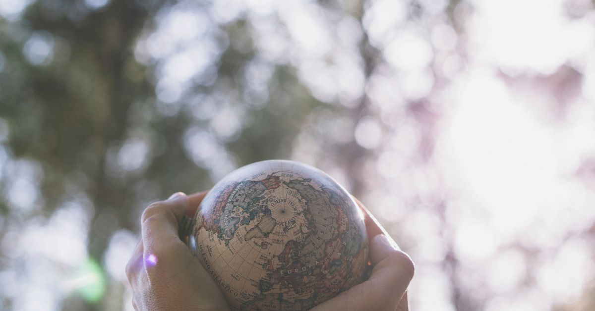 Mãos segurando um pequeno globo terrestre com fundo natural, representando a adaptação da saúde ao clima.