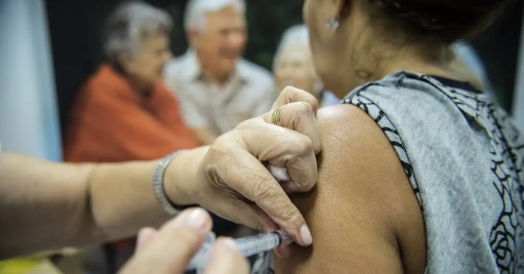 Profissional de saúde aplica vacina em mulher adulta durante campanha de imunização no Brasil.