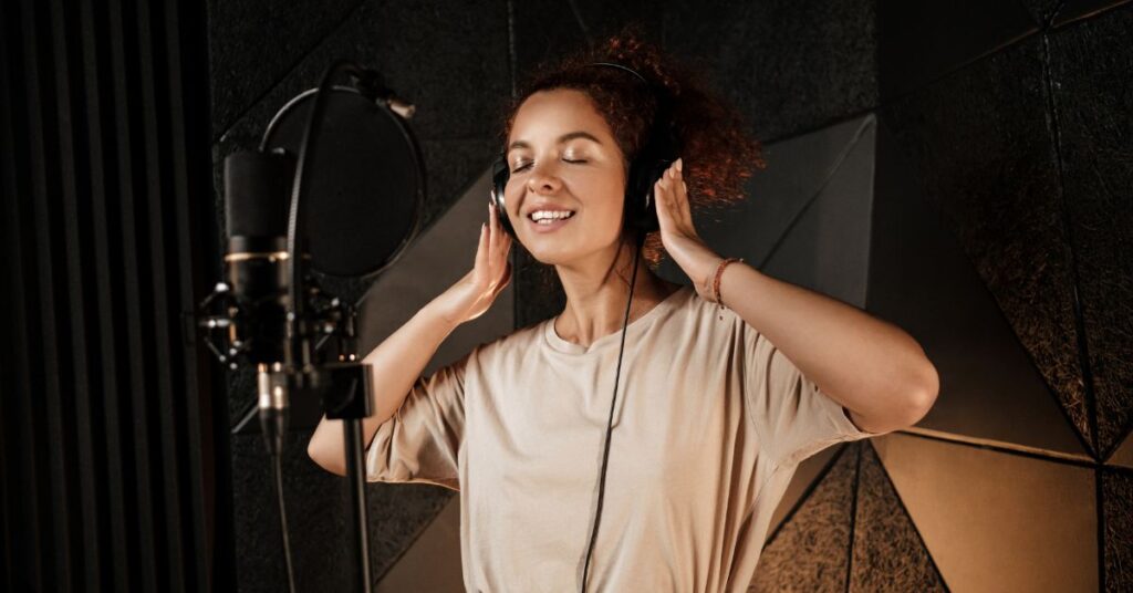 mulher cantando com fones de ouvido em estúdio, representando os benefícios do canto.