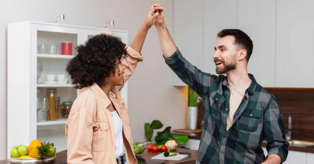 leituras sobre relacionamentos - Casal sorridente dançando juntos na cozinha, representando alegria e harmonia nas relações.