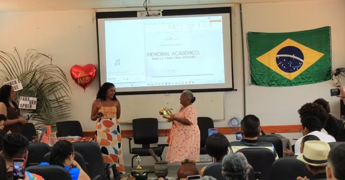 Idosa apresenta o TCC na UFNT segurando saxofone ao lado da orientadora, durante defesa de Maria de Fátima TCC