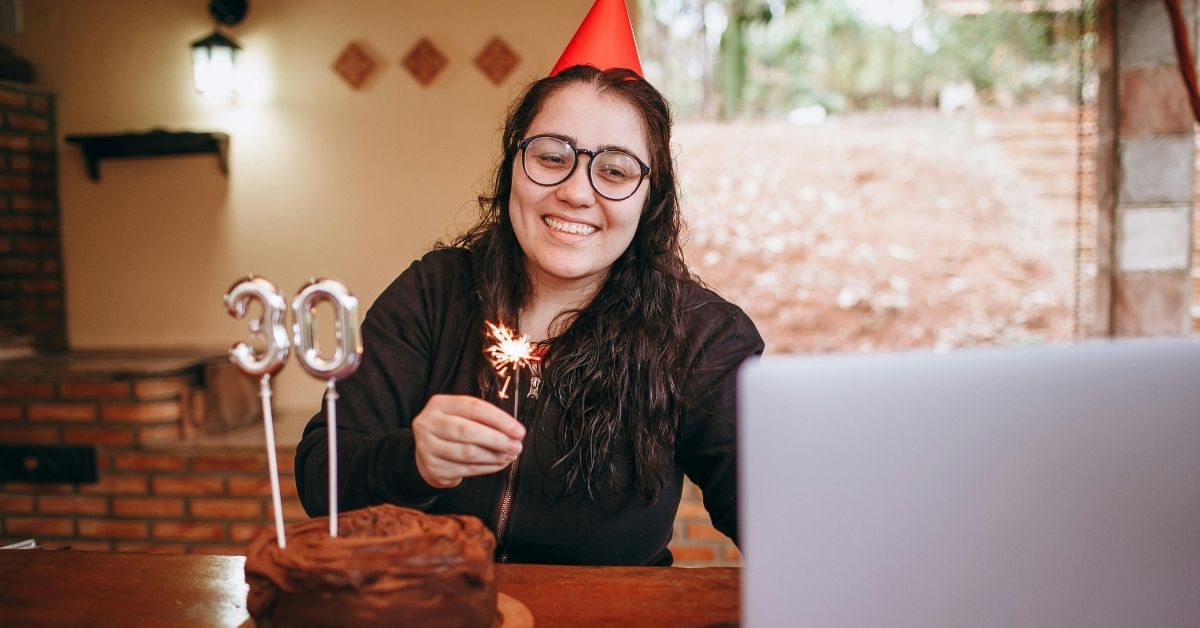 Mulher celebrando aniversário de 30 anos durante chamada de vídeo, ilustrando estudo de Cambridge sobre o fim da adolescência aos 32 anos.