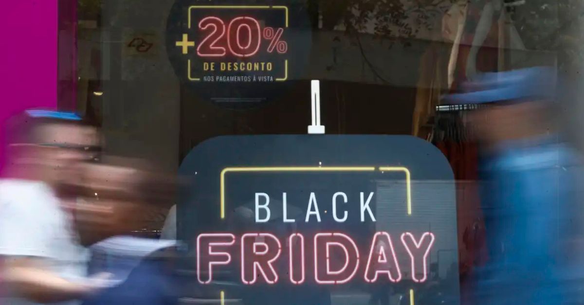Vitrine com anúncio de descontos da Black Friday Brasil e pessoas passando em frente à loja.