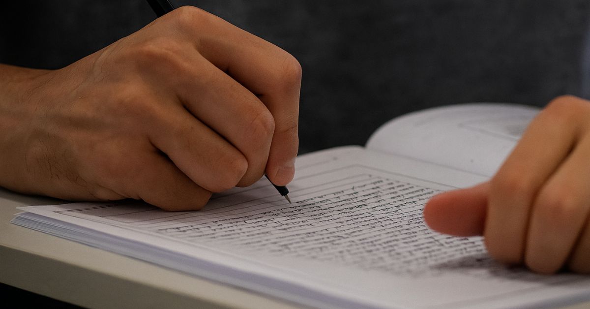 redação do Enem sobre envelhecimento - Mão de estudante escrevendo em caderno durante a redação do Enem 2025.