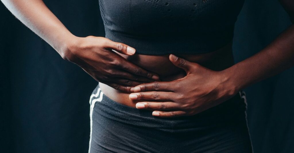 Pessoa tocando o abdômen para ilustrar desconforto e a importância dos alimentos para desinchar.