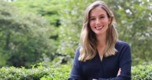 Retrato de Luana Lara Lopes, bilionária mais jovem do mundo, sorrindo em área externa com vegetação ao fundo.