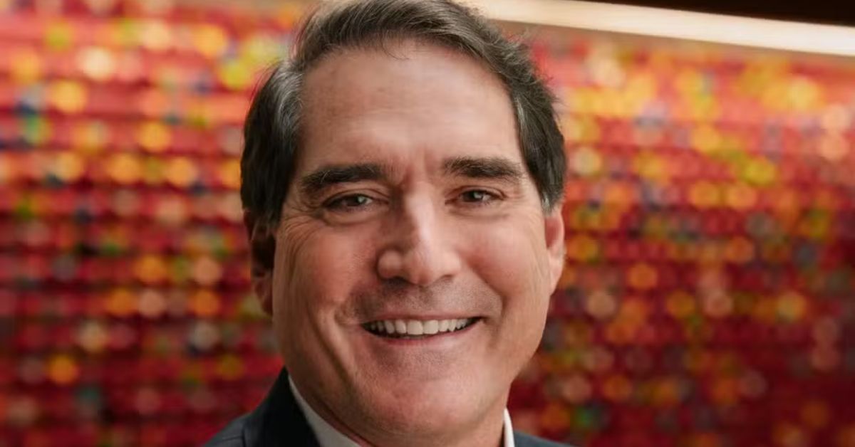 Brasileiro CEO da Coca-Cola sorri em retrato oficial com fundo colorido.