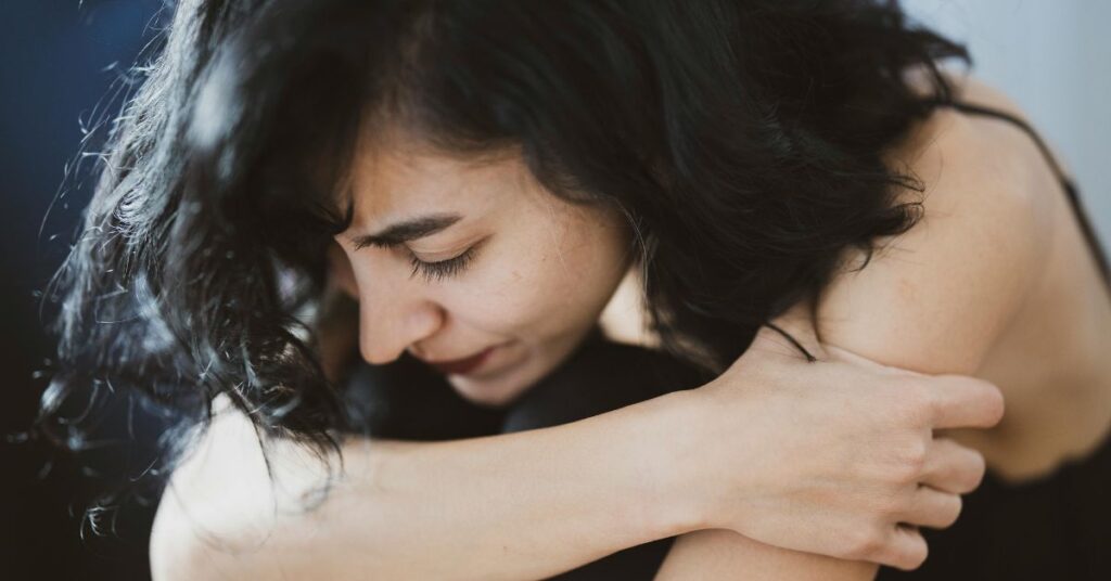 Mulher sentada na cama durante crise de ansiedade à noite, tentando se acalmar antes de dormir