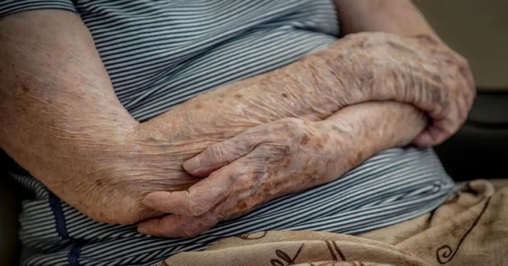 “Mãos de uma pessoa idosa entrelaçadas, ilustrando impactos da doença de Parkinson no cotidiano.”