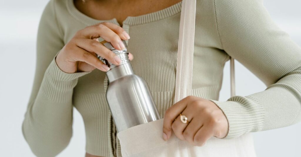 Pessoa guardando uma garrafa de inox na bolsa, reforçando a higiene da garrafinha d’água no dia a dia.
