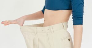 "Pessoa segurando calça larga após emagrecer, ilustrando como padrões emocionais influenciam no emagrecimento."