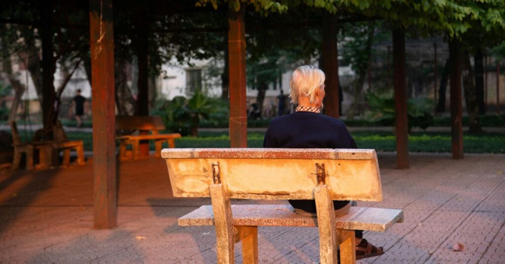 Idoso sentado em banco de praça durante o entardecer, em cena que simboliza iniciativas de prevenção da demência.