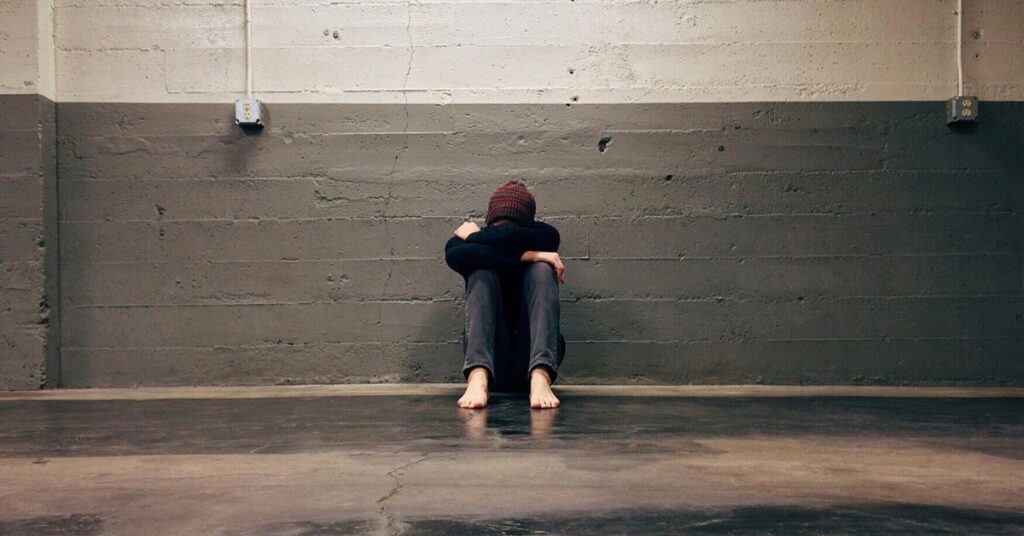 Pessoa sentada no chão, abraçando as pernas, ilustrando sofrimento emocional ligado ao tratamento para depressão.