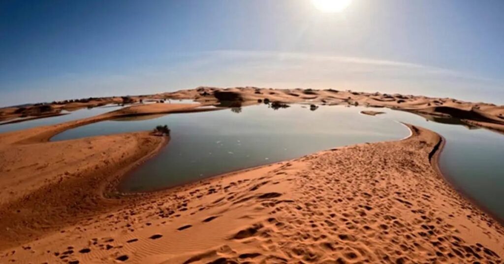 Água no deserto do Saara forma lago entre dunas sob sol intenso
