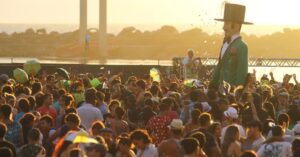 previsão do tempo no Carnaval com foliões sob sol e nuvens em capital brasileira