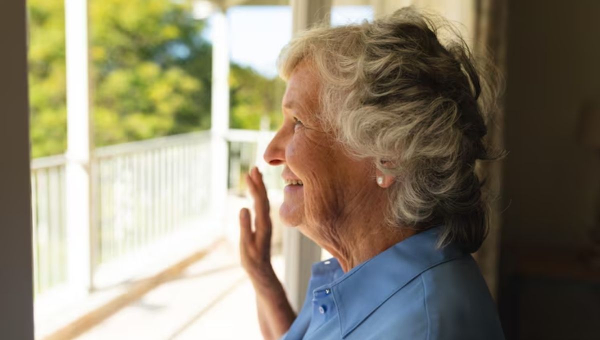 idosa em casa sorrindo perto da janela representando atendimento domiciliar para idosos