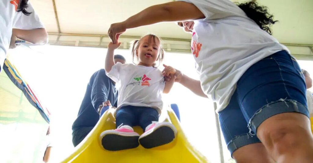 criança com síndrome de Down em atividade recreativa com apoio de educadora