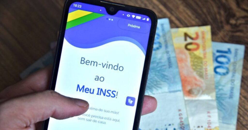 Pessoa consultando o 13º do INSS pelo aplicativo Meu INSS no celular com notas de real ao fundo