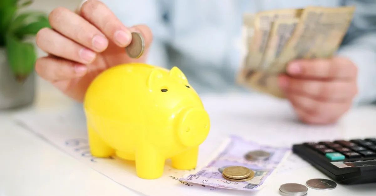 Pessoa colocando moeda em cofrinho enquanto organiza dinheiro como prática de educação financeira