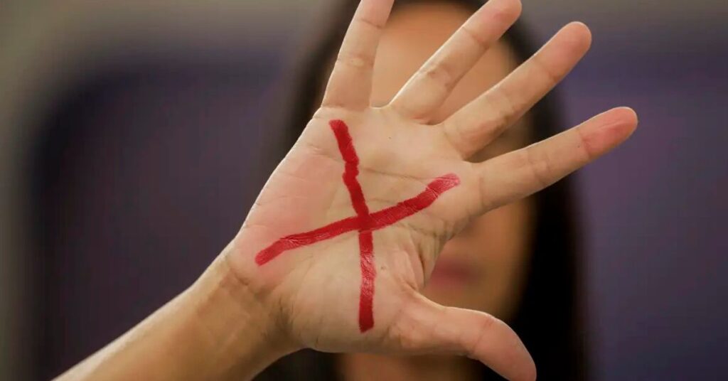 Mulher levanta a mão com símbolo em vermelho representando leis de proteção a mulher e combate à violência