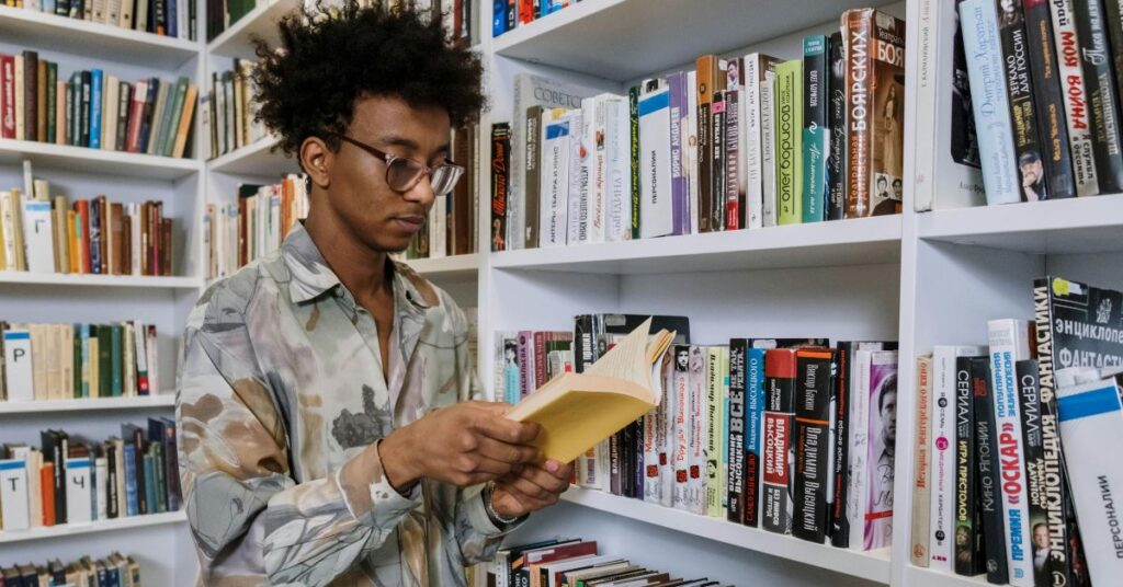 Jovem lendo livro em biblioteca, representando diversidade cultural e formação de novos escritores no Brasil