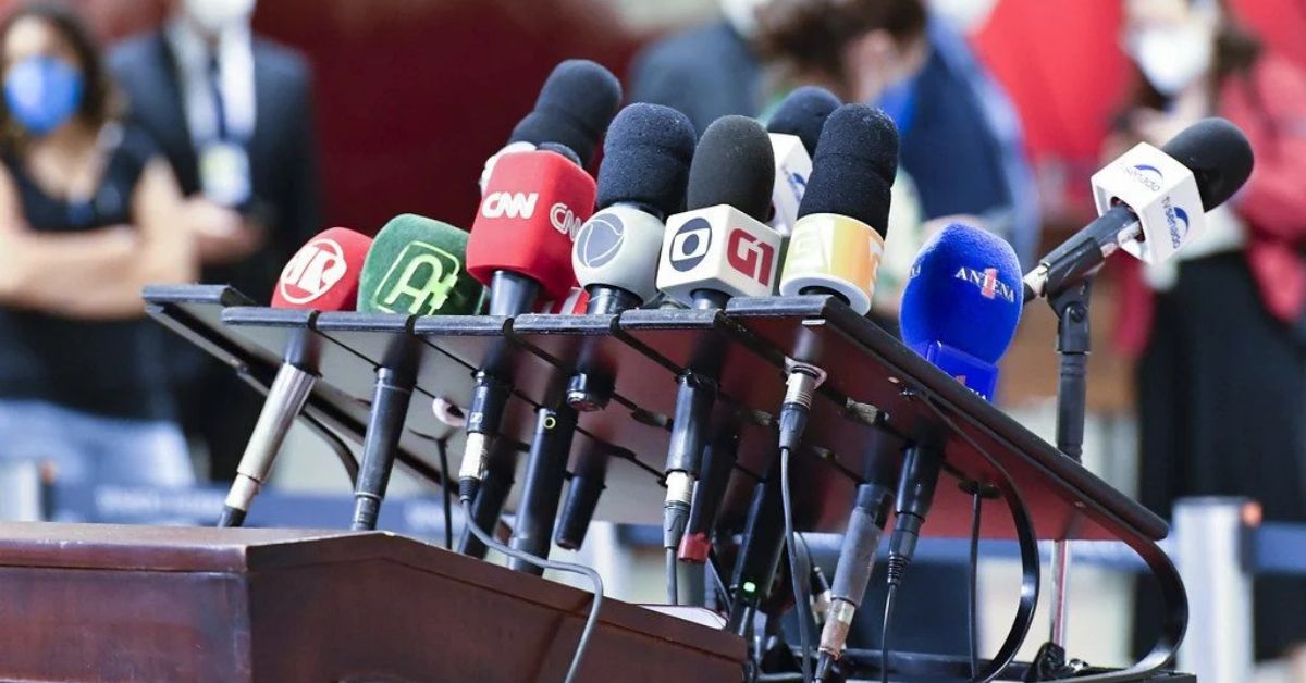 Coletiva de imprensa com microfones de veículos de comunicação representando a proteção a jornalistas no Brasil