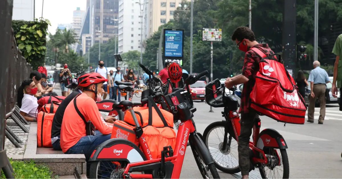Entregadores de aplicativo com bicicletas elétricas e mochilas de entrega durante atividade urbana após anúncio de crédito para entregadores de aplicativo