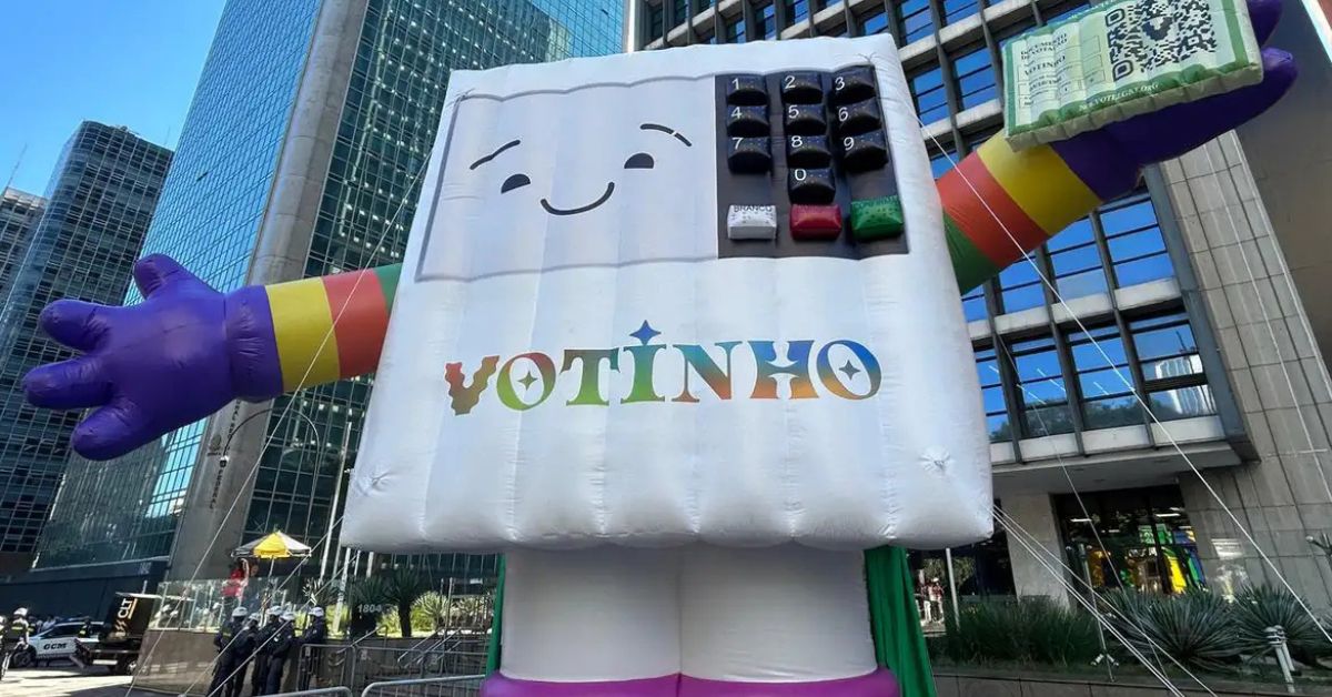 Boneco inflável em formato de urna eletrônica com as cores do arco-íris na Avenida Paulista durante a Parada LGBT São Paulo 2026, que destacou a importância do voto e dos direitos LGBTQIA+ no Brasil.