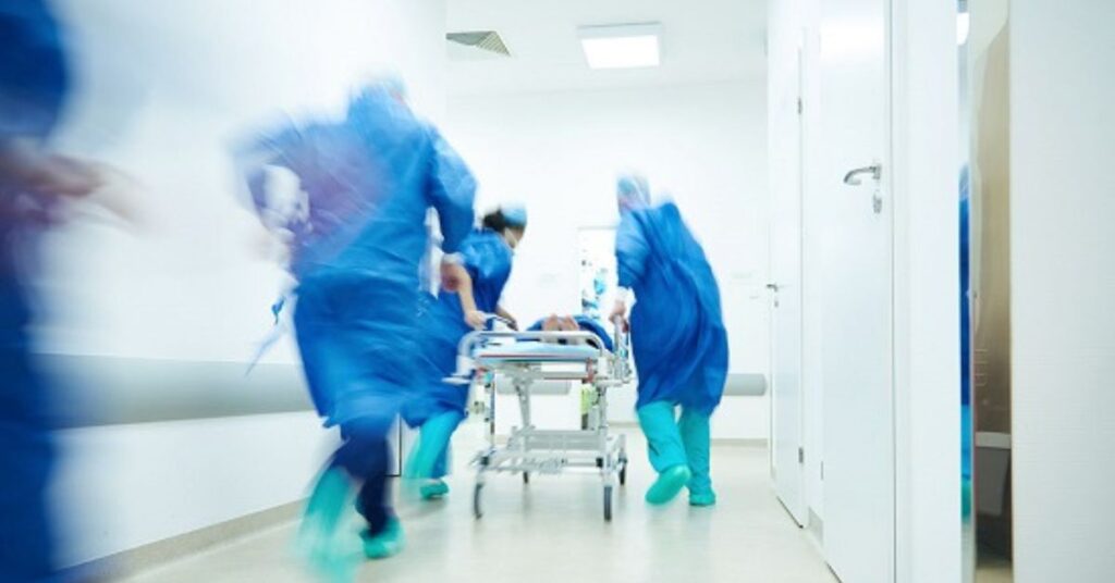 Equipe médica transporta paciente em hospital durante atendimento de emergência, ilustrando ações de resposta a emergências em saúde pública no Brasil.