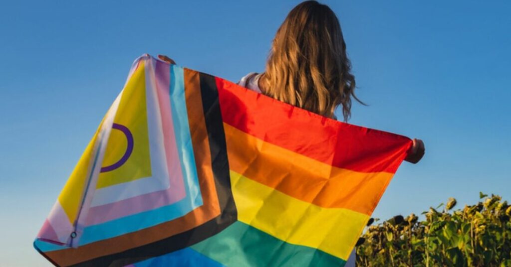 Pessoa segurando bandeira LGBTQIA+ durante ação que representa políticas públicas para população LGBTQIA+, inclusão social, acolhimento e geração de oportunidades.