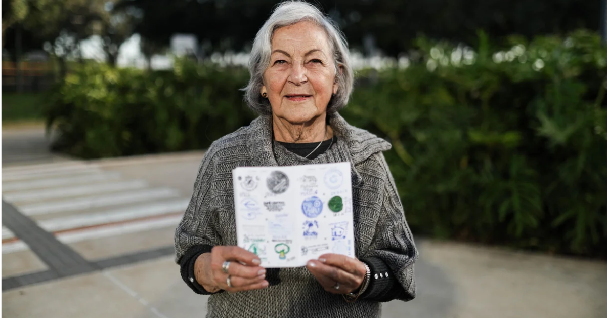 Marlene Terezinha de Carvalho Leite segura a Compostela, certificado do Caminho de Santiago, durante registro ao ar livre após concluir a peregrinação.