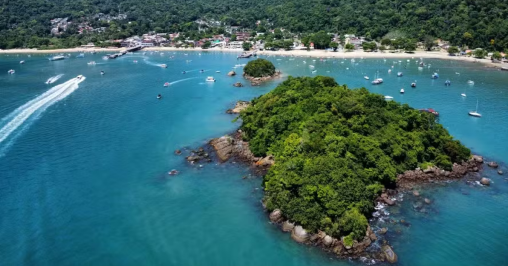 Vista aérea da Ilha Grande, no litoral sul do Rio de Janeiro, com águas azul-turquesa, áreas de Mata Atlântica, embarcações e faixa de praia ao fundo.