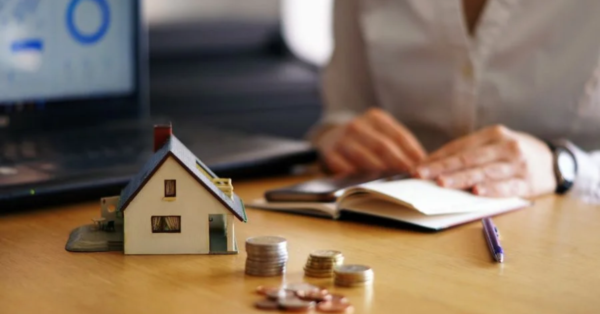 Miniatura de uma casa e moedas sobre mesa representam financiamento imobiliário após novo corte da Selic.
